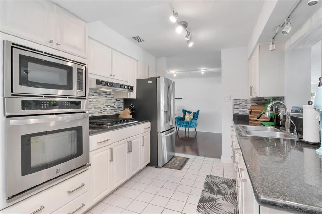 A kitchen features white cabinets, stainless steel appliances, dark granite countertops, and white tile flooring — 3991 38TH WAY S, ST PETERSBURG, FL