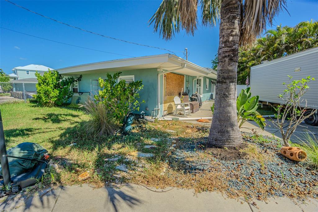 A teal single-story house with a boarded-up window and a palm tree in the yard — 16101 4TH STREET E, REDINGTON BEACH, FL