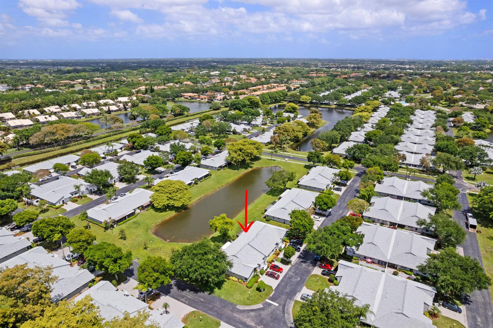 An aerial view shows a residential community with grey-roofed buildings surrounding a central pond — 8955 Windtree Street # C, Boca Raton FL 33496, BOCA RATON, FL