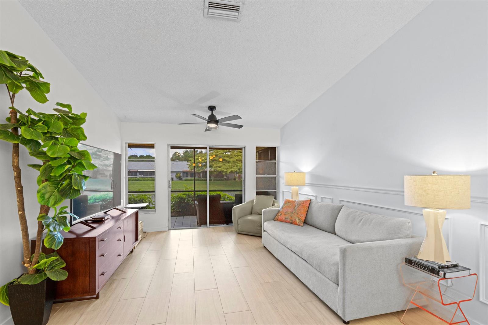 A living room features light wood-look tile flooring, a gray sofa, and a sliding glass door — 8955 Windtree Street # C, Boca Raton FL 33496, BOCA RATON, FL