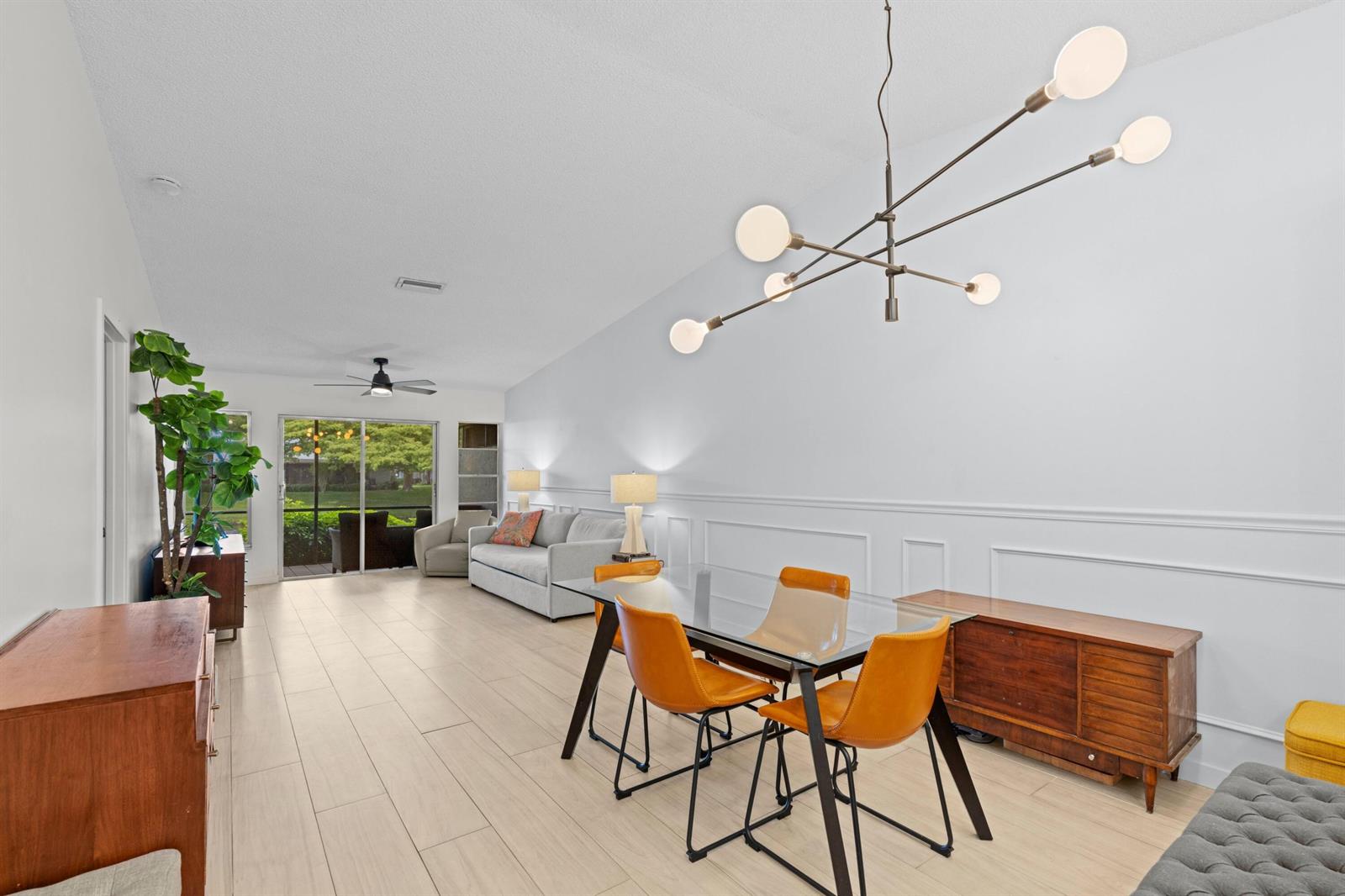 A bright living and dining area features a glass table, mid-century furniture, and tile flooring — 8955 Windtree Street # C, Boca Raton FL 33496, BOCA RATON, FL