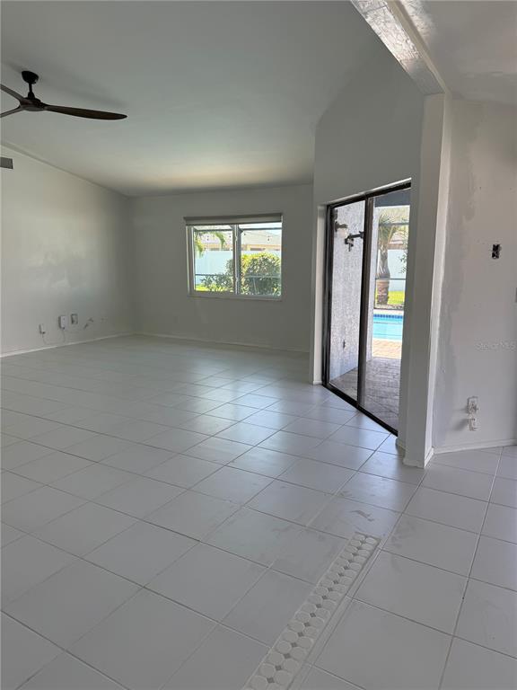 An empty living room with white tile floors, a ceiling fan, and sliding glass doors — 32 NE 13TH PLACE, CAPE CORAL, FL