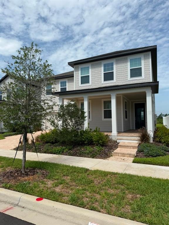A two-story house with a covered front porch, light siding, and a paved walkway — 17658 JAPONICA BLOOM DRIVE, WINTER GARDEN, FL
