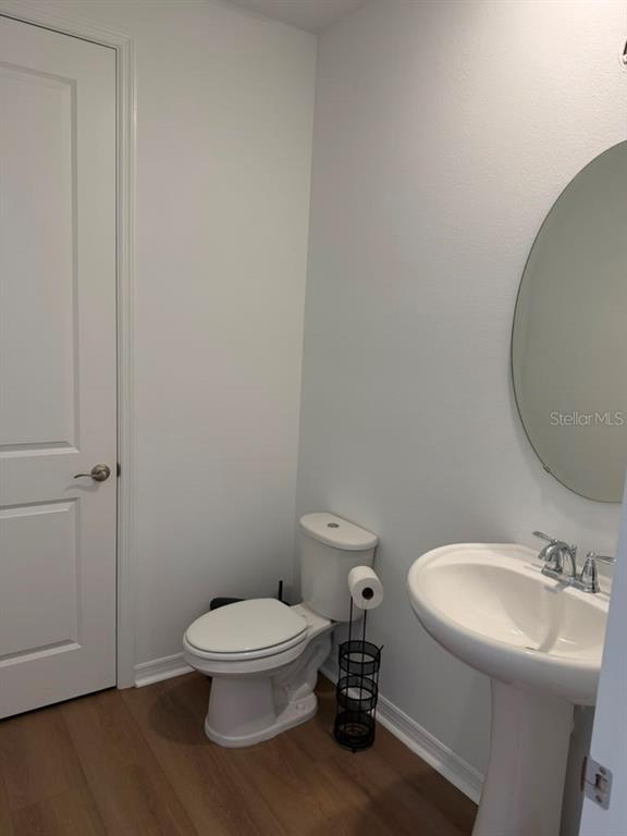 A small bathroom features a pedestal sink, a toilet, and a round wall mirror — 17658 JAPONICA BLOOM DRIVE, WINTER GARDEN, FL