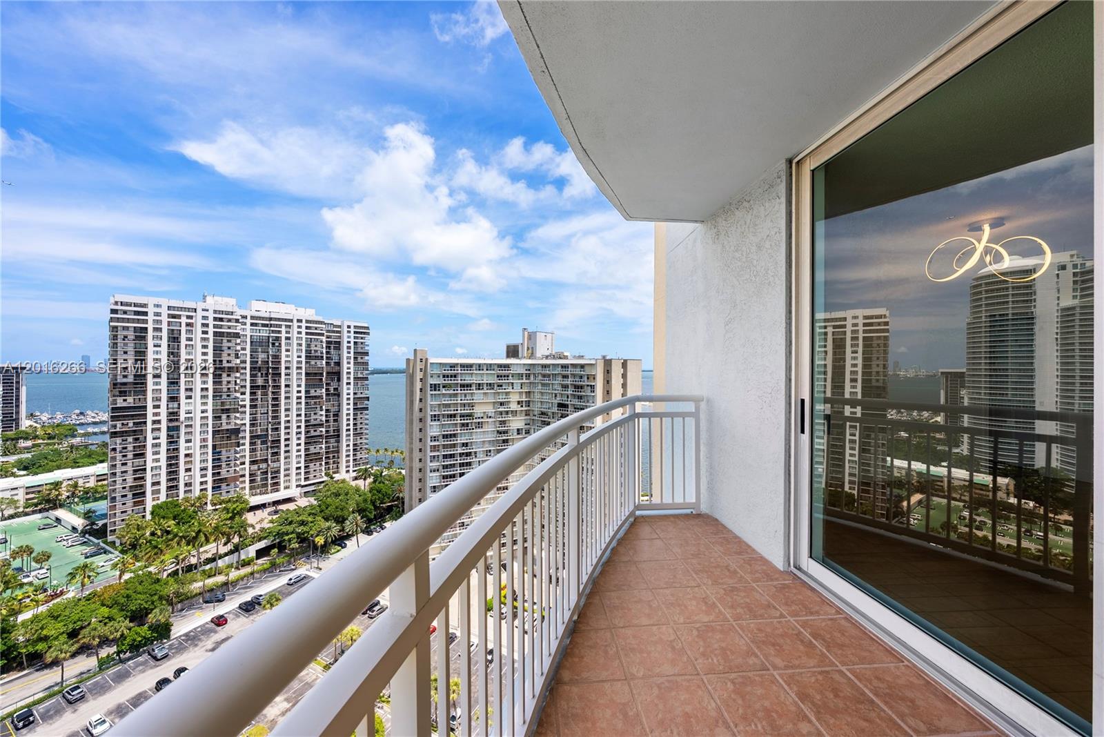 A high-rise balcony with tiled flooring overlooks a city street, nearby buildings, and the water — 2475 Brickell Ave # 2206, Miami FL 33129, MIAMI, FL