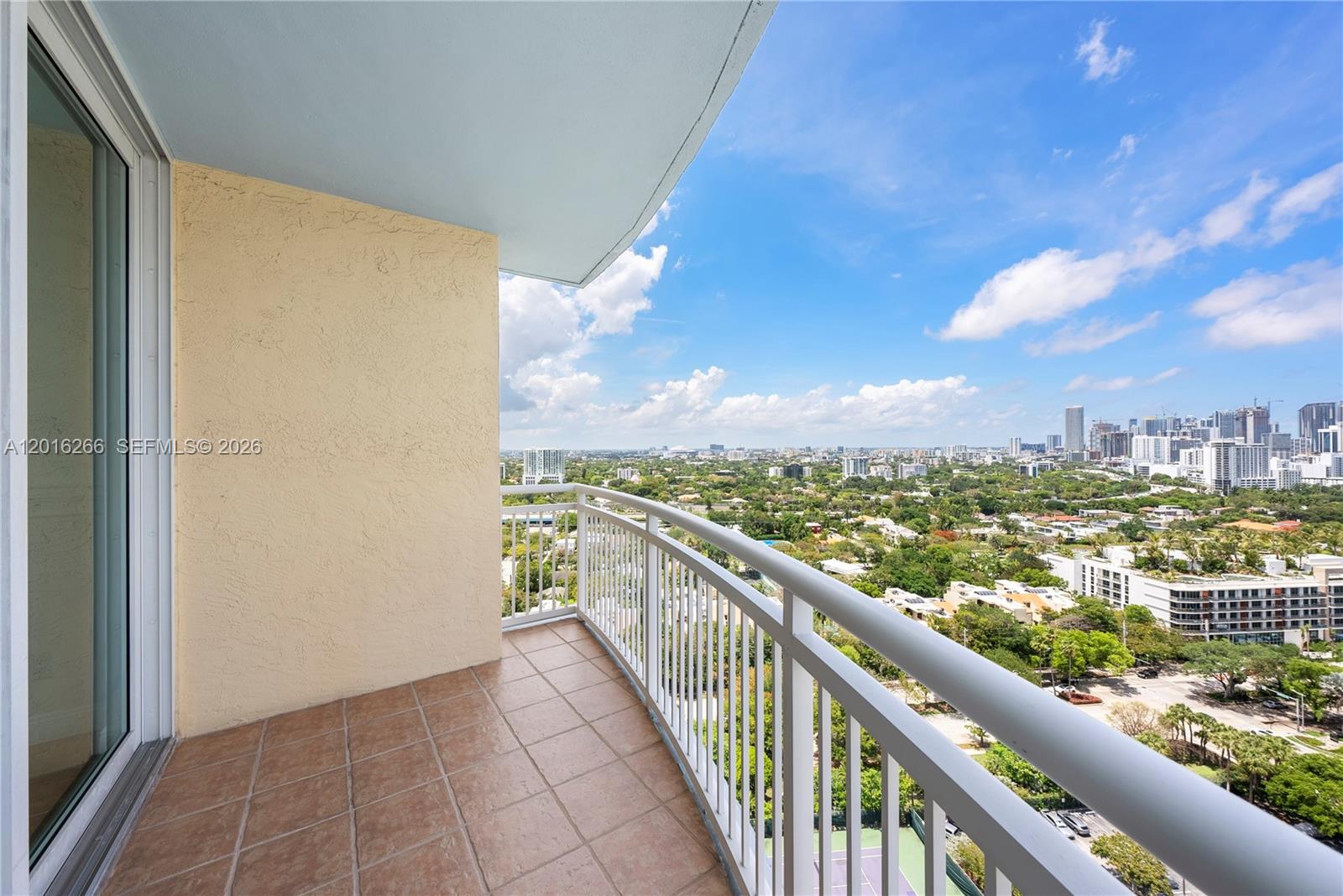 A tiled balcony with a white metal railing overlooks a city skyline and green trees — 2475 Brickell Ave # 2206, Miami FL 33129, MIAMI, FL