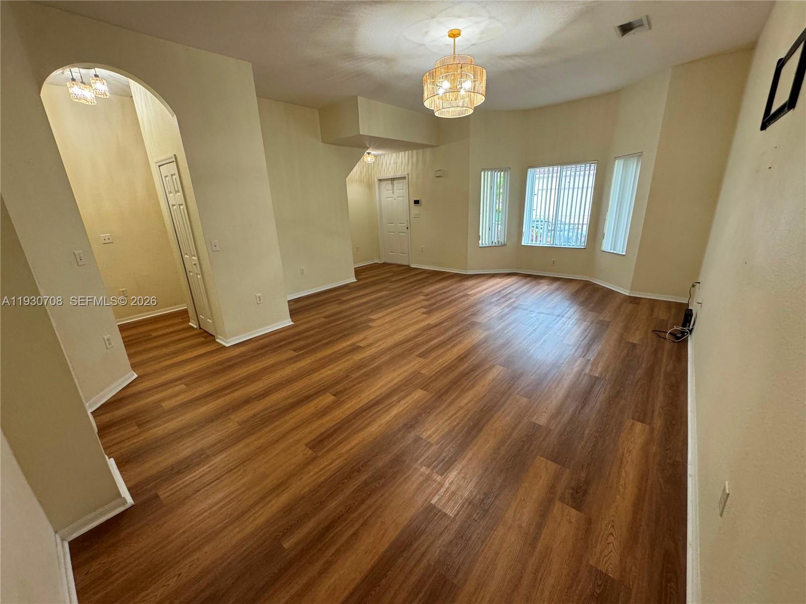 An empty living room features wood-look flooring, a chandelier, and a bay window — 2452 SE 19th Ct, Homestead FL 33035, HOMESTEAD, FL
