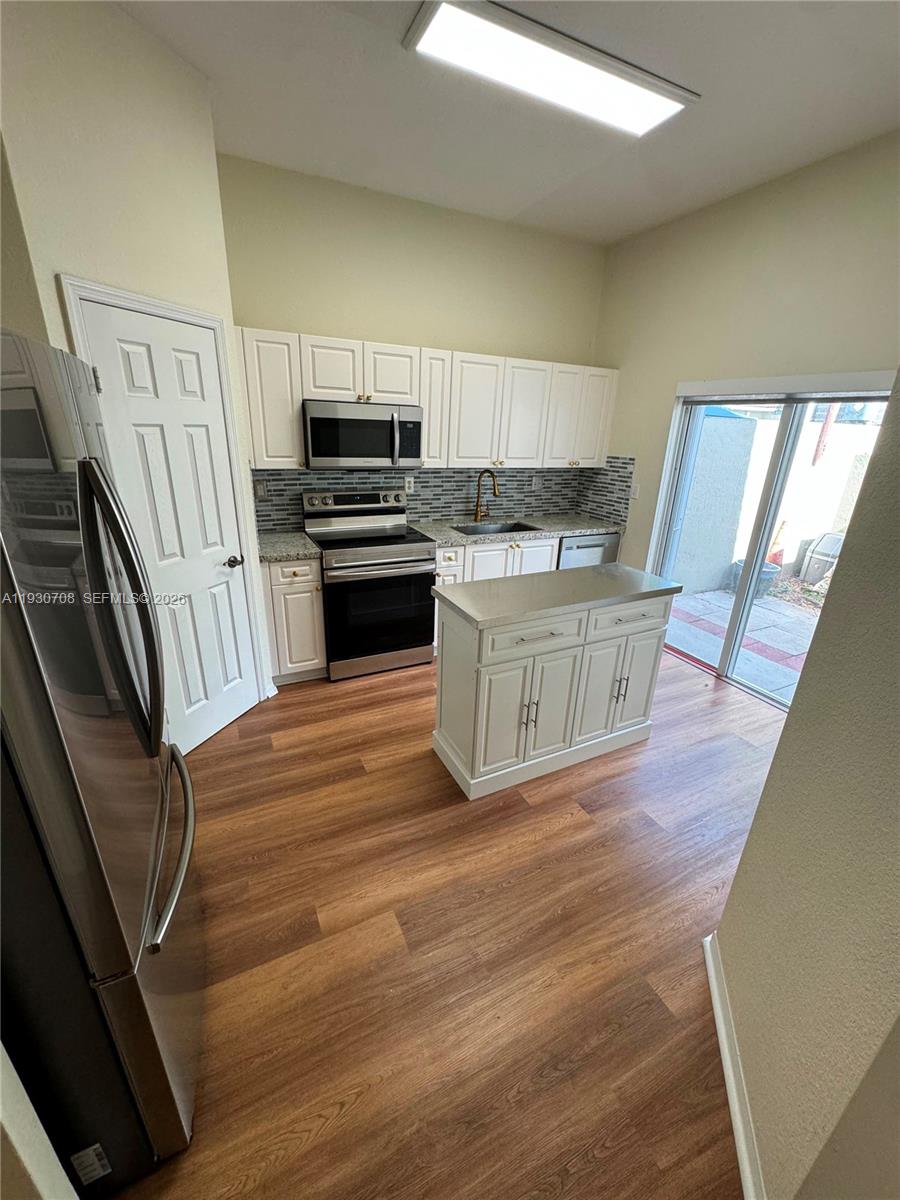 A kitchen features white cabinetry, stainless steel appliances, a center island, and wood-look flooring — 2452 SE 19th Ct, Homestead FL 33035, HOMESTEAD, FL