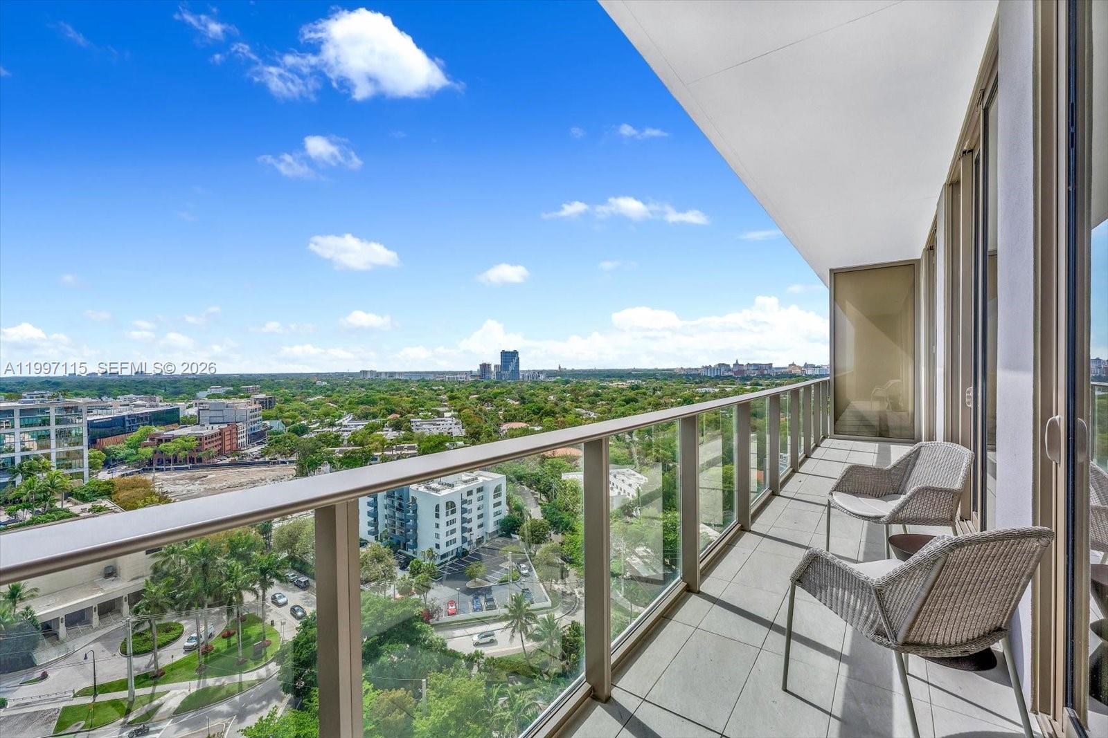 A high-rise balcony features a glass railing, two wicker chairs, and an expansive city view — 2678 Tigertail Ave # 1505, Miami FL 33133, MIAMI, FL