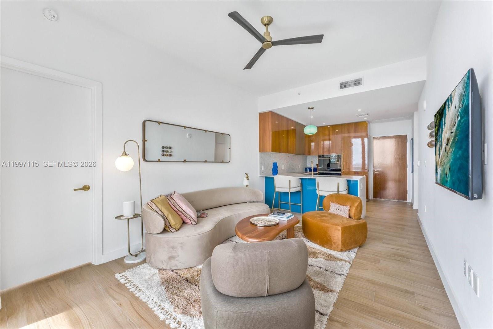 This living room features a curved sofa, two armchairs, and an open-concept kitchen with blue cabinets — 2678 Tigertail Ave # 1505, Miami FL 33133, MIAMI, FL