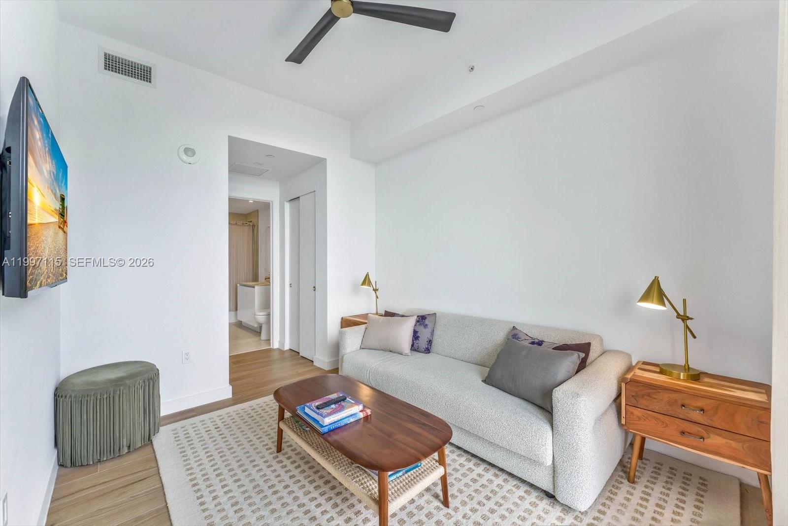 A living room features a light gray sofa, a wooden coffee table, and a television — 2678 Tigertail Ave # 1505, Miami FL 33133, MIAMI, FL