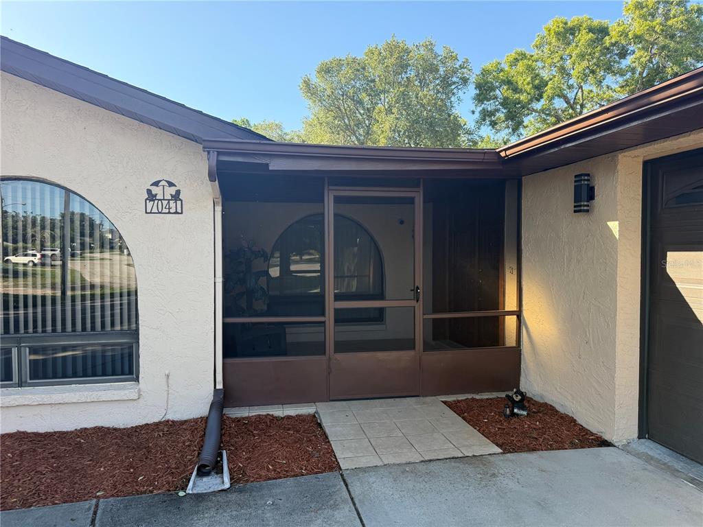 The exterior view shows a house entrance with a screened porch and a concrete walkway — 7041 MAYHILL COURT, SPRING HILL, FL