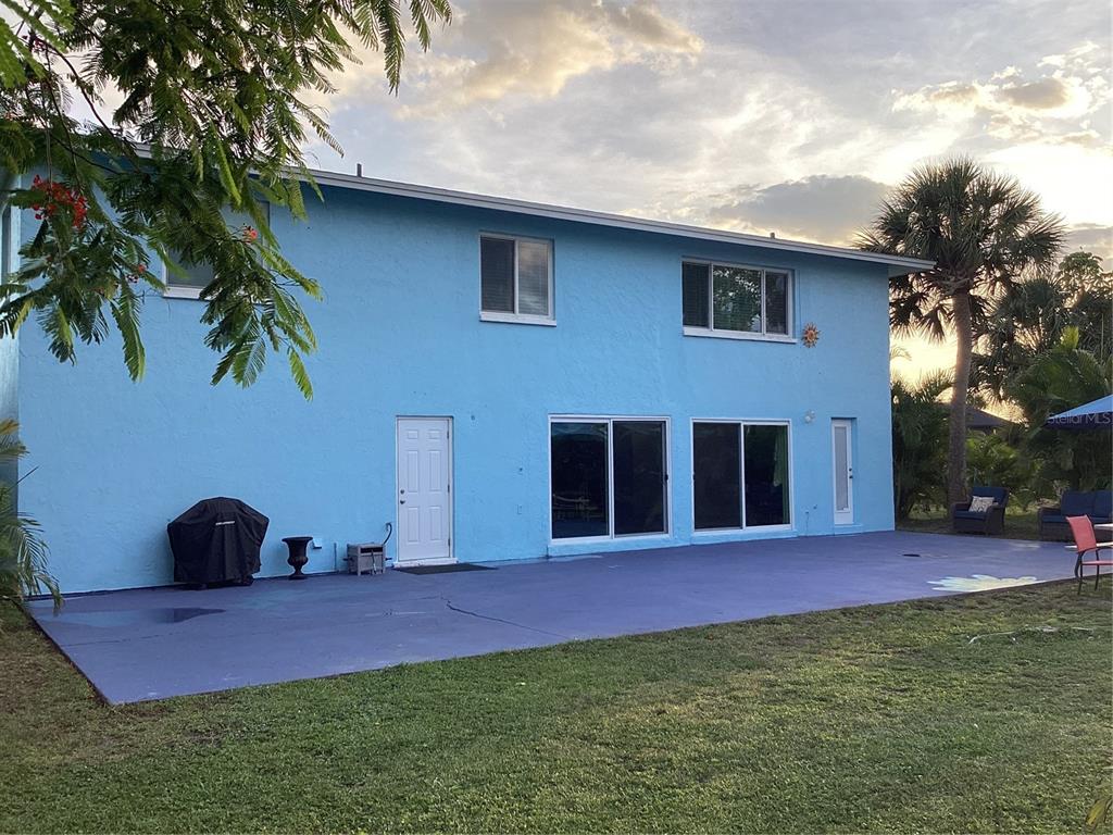 The exterior of a two-story blue house features a large patio and sliding glass doors — 90 OAKLAND HILLS COURT, ROTONDA WEST, FL