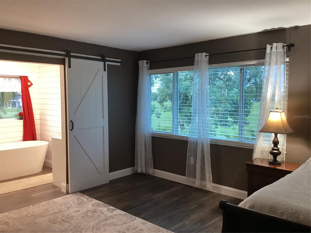 A bedroom with dark walls, wood-look flooring, a sliding barn door, and an attached bathroom — 90 OAKLAND HILLS COURT, ROTONDA WEST, FL