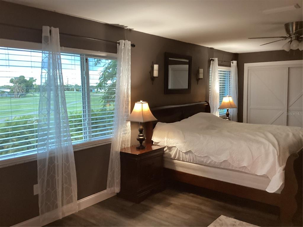 A bedroom features dark walls, a wooden bed frame, two lamps, and large windows — 90 OAKLAND HILLS COURT, ROTONDA WEST, FL