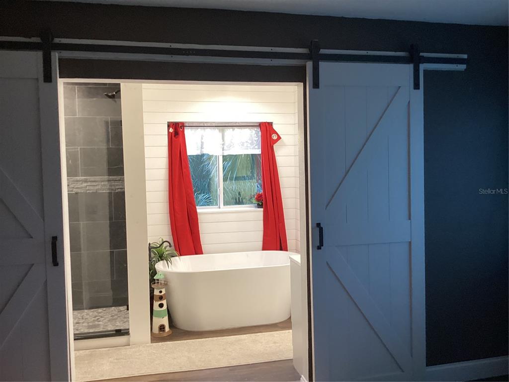 A bathroom with a freestanding tub and walk-in shower viewed through white sliding barn doors — 90 OAKLAND HILLS COURT, ROTONDA WEST, FL