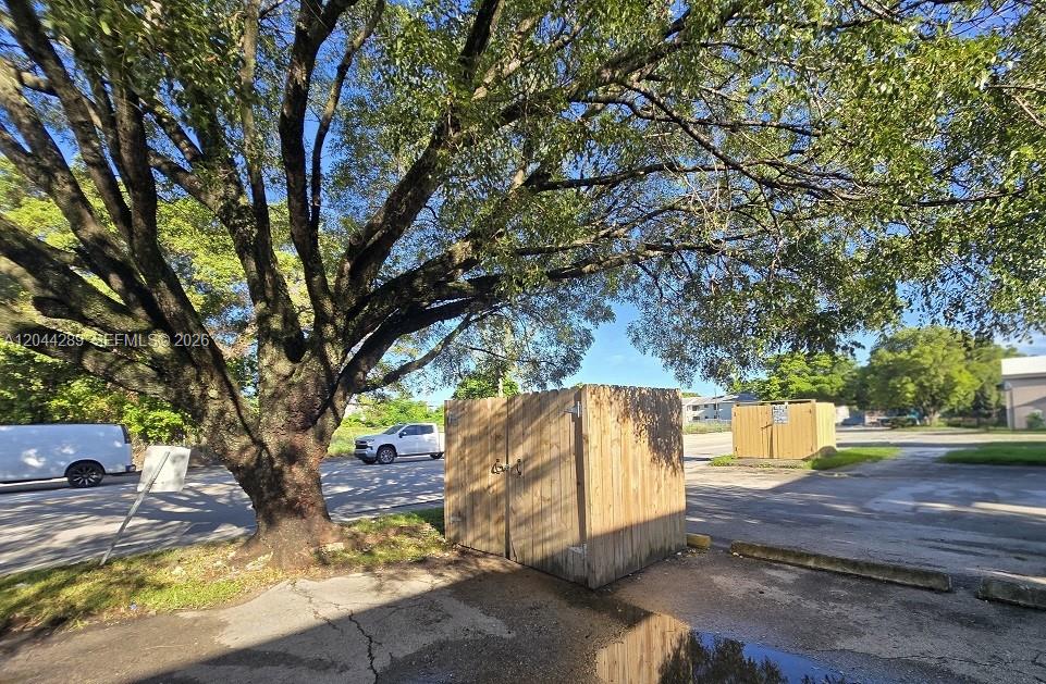 A large tree stands next to two wooden trash enclosures in a paved parking lot — 2835 NW 22nd Ave, Miami FL 33142, MIAMI, FL