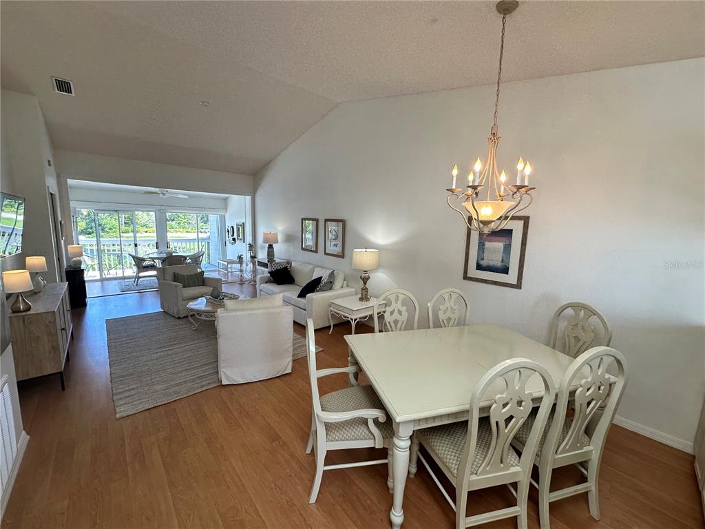 A dining area with a chandelier and a living room with vaulted ceilings and wood floors — 517 WOODSTORK CIRCLE, BRADENTON, FL