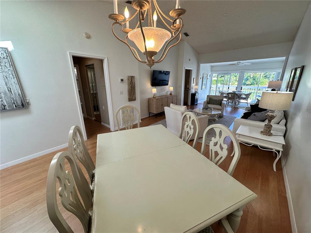 A dining area with a chandelier overlooks a living room and a sunlit patio — 517 WOODSTORK CIRCLE, BRADENTON, FL