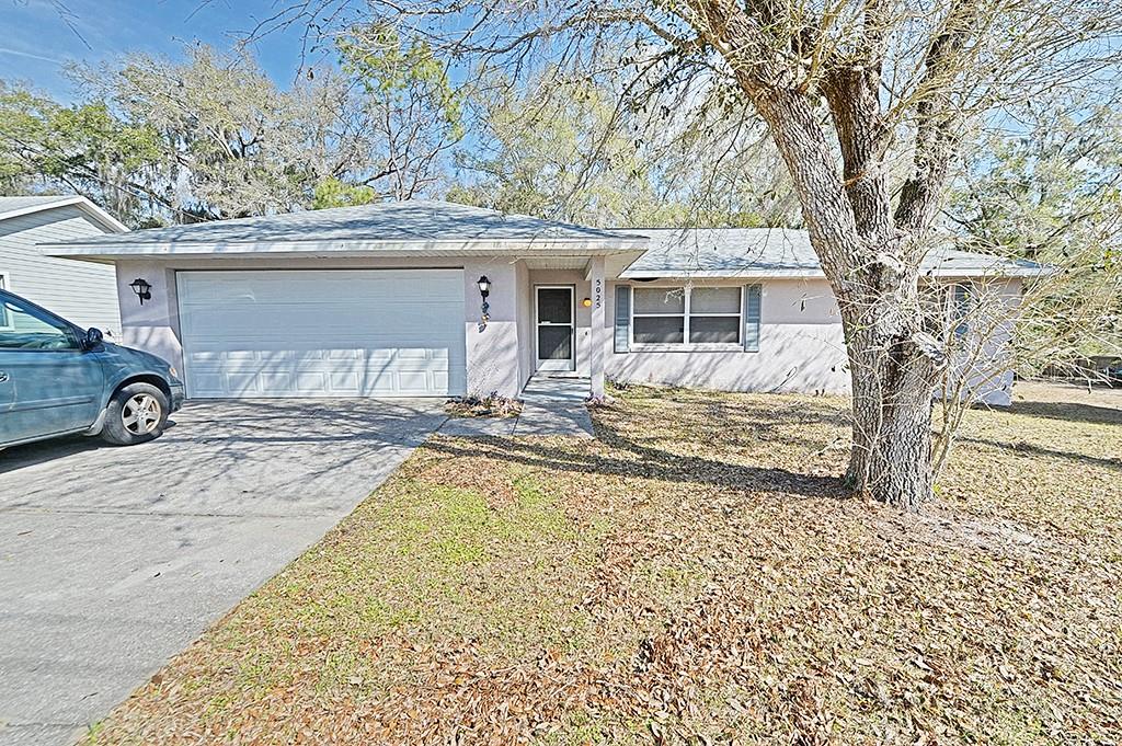 A single-story house with a two-car garage, light-colored siding, and a large front tree — 5025 S HUMMINGBIRD AVENUE, INVERNESS, FL