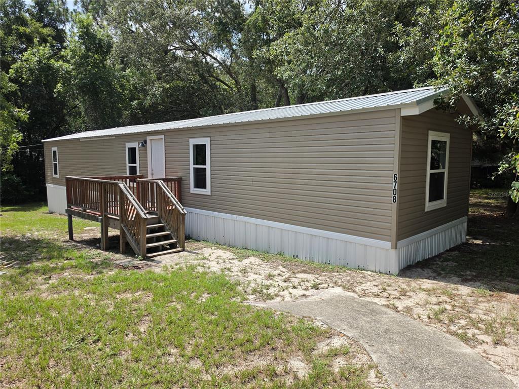 A tan mobile home with a wooden deck and a metal roof sits on grass — 6708 W CHERRYWOOD COURT, CRYSTAL RIVER, FL