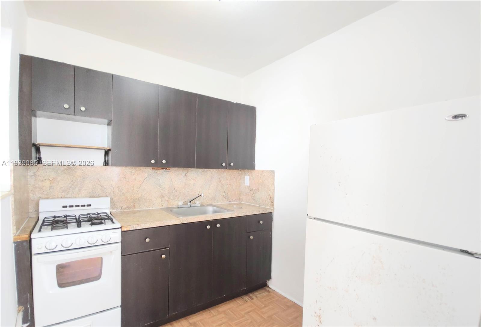 A kitchen features dark brown cabinets, a white stove, a white refrigerator, and stone countertops — 1565 SW 6th St, Miami FL 33135, MIAMI, FL