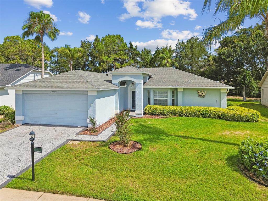 A light blue single-story house features a two-car garage and a landscaped front yard — 10919 TRELAIN WAY, HUDSON, FL