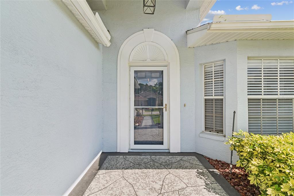 The exterior entrance features a glass storm door, an arched transom, and a paved porch — 10919 TRELAIN WAY, HUDSON, FL