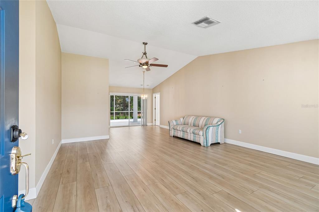 A living room with light wood-look flooring, beige walls, a vaulted ceiling, and a sofa — 10919 TRELAIN WAY, HUDSON, FL