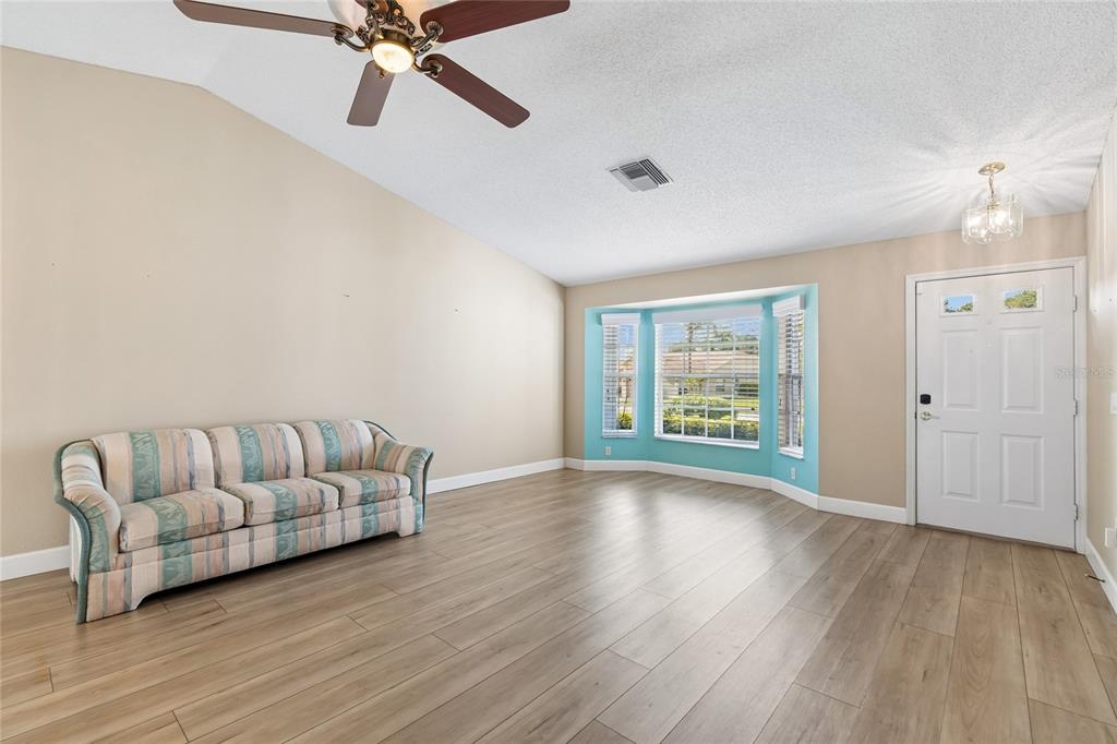 A living room with light wood flooring, a striped sofa, and a bay window — 10919 TRELAIN WAY, HUDSON, FL