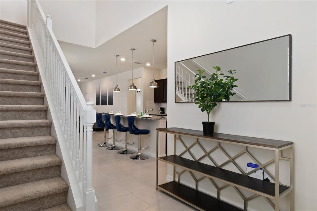 A carpeted staircase leads to an open-concept kitchen with bar seating and a console table — 4428 KAIPO ROAD, DAVENPORT, FL
