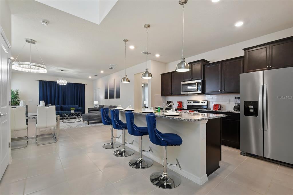 A modern kitchen features dark wood cabinets, granite countertops, and blue bar stools at an island — 4428 KAIPO ROAD, DAVENPORT, FL
