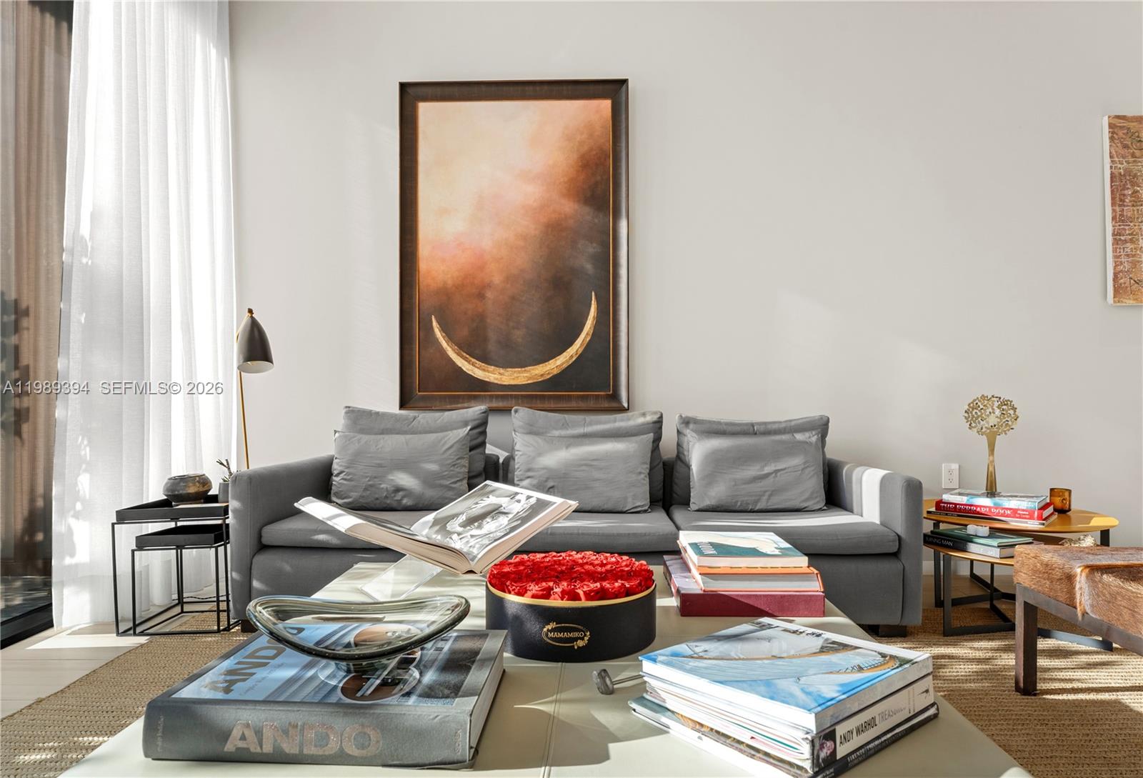A living room features a gray sofa, a large crescent moon painting, and coffee table books — 3156 SW 27th Ave # 202, Miami FL 33133, MIAMI, FL