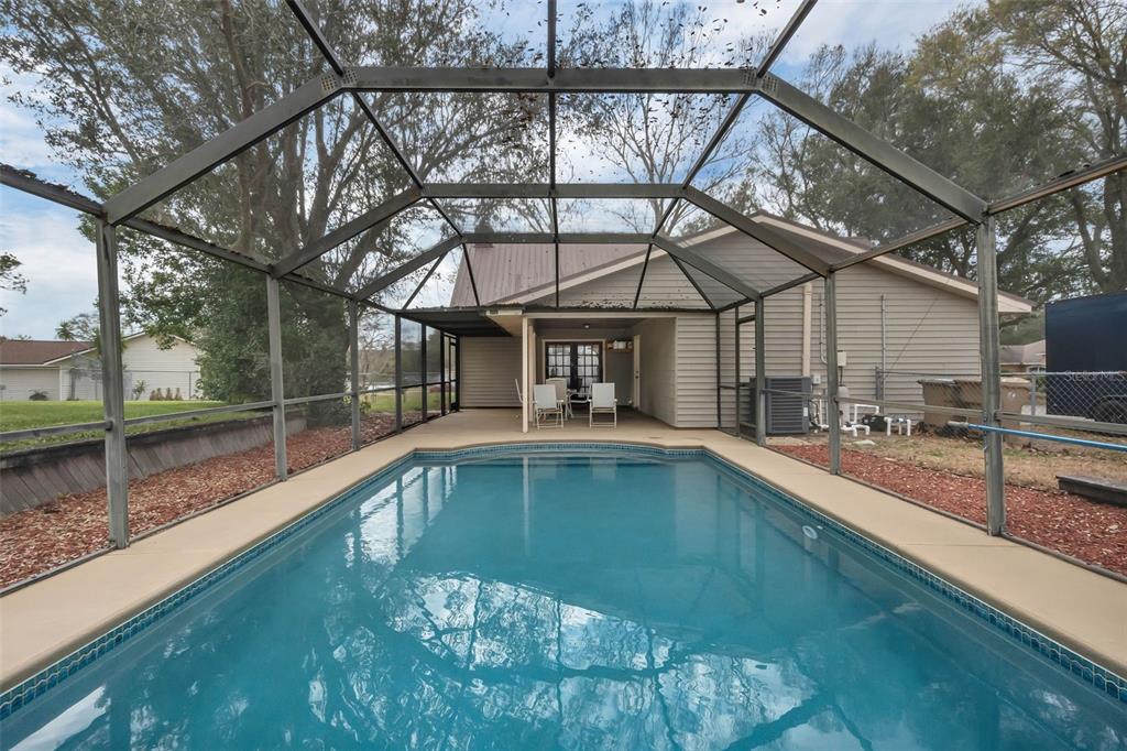 A swimming pool sits inside a screened-in lanai behind a single-story house — 9610 NELLIE HILLS COURT, CLERMONT, FL