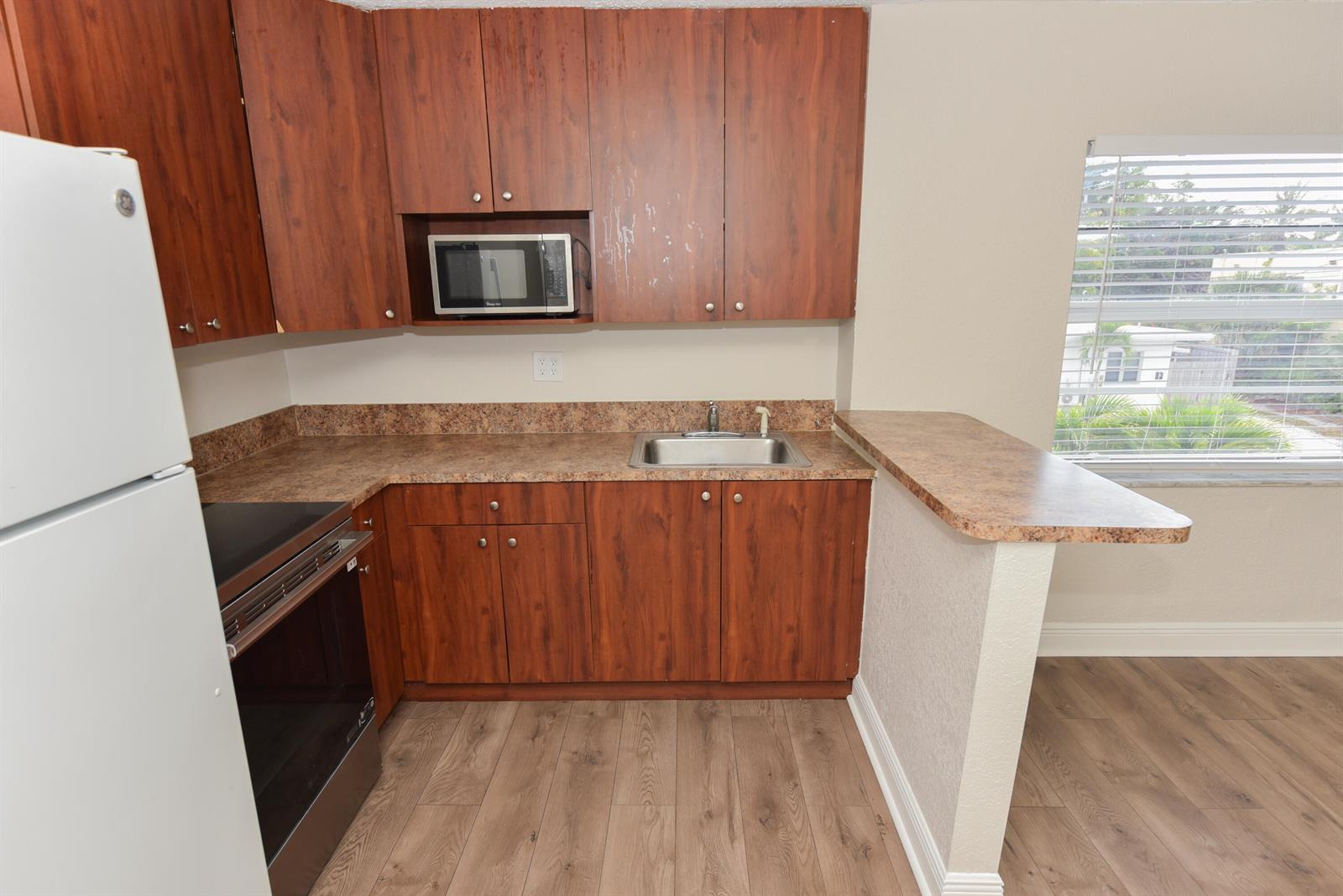 A kitchen features wood-grain cabinets, a microwave, a stainless steel sink, and a breakfast bar — 605 N Federal Highway # 9, FL 33460, FL
