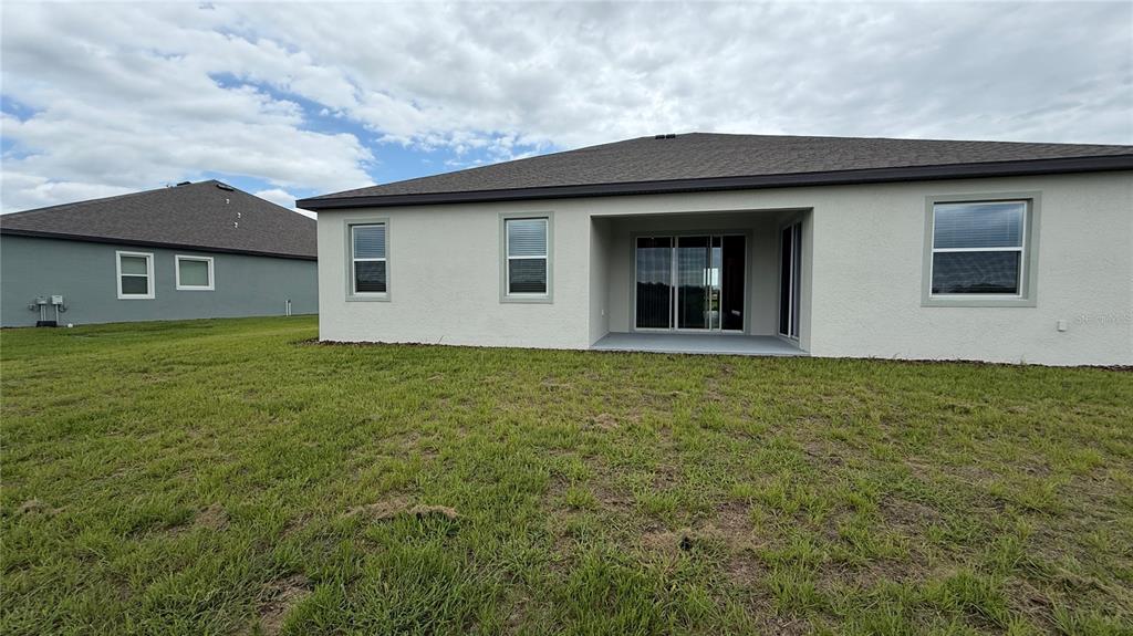 The rear exterior of a single-story house features a covered patio and a grassy yard — 4378 WINESAP WAY, LAKELAND, FL