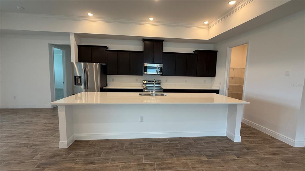 A kitchen features a large white island, dark wood cabinets, and stainless steel appliances — 4378 WINESAP WAY, LAKELAND, FL