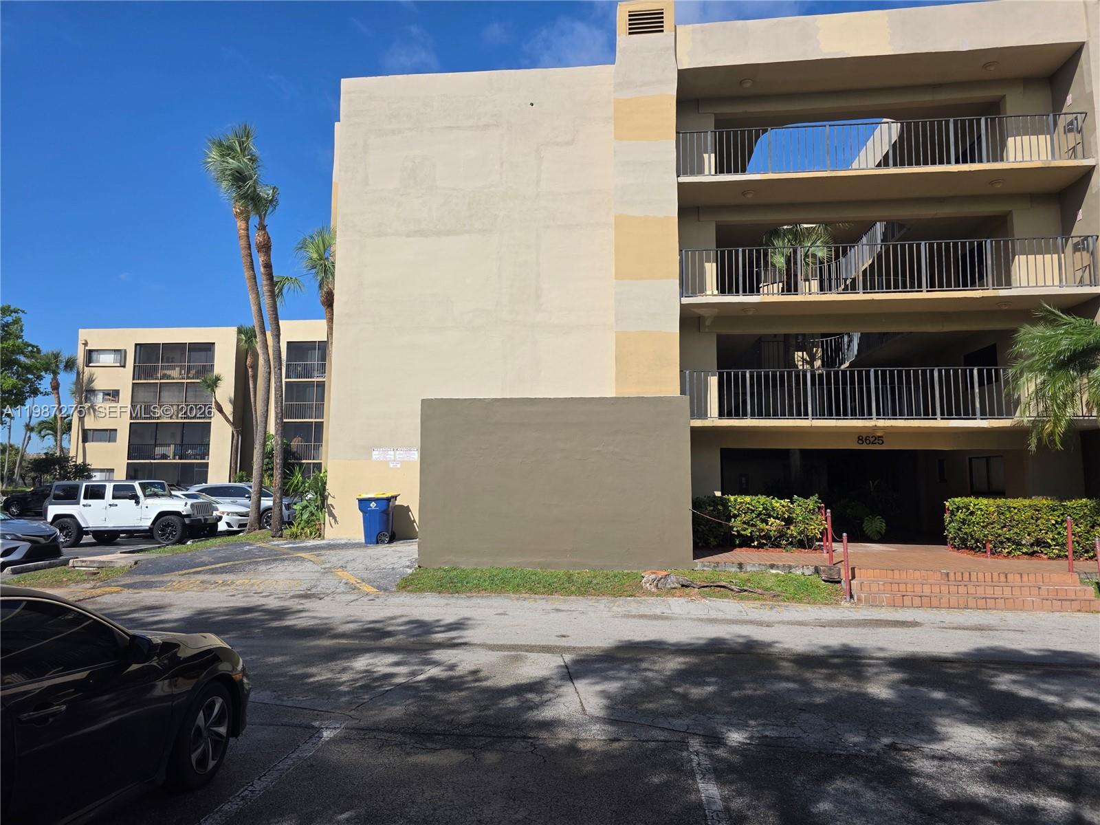 Exterior view of a multi-story apartment building with balconies and a parking lot — 8615 NW 8th St # 319, Miami FL 33126, MIAMI, FL