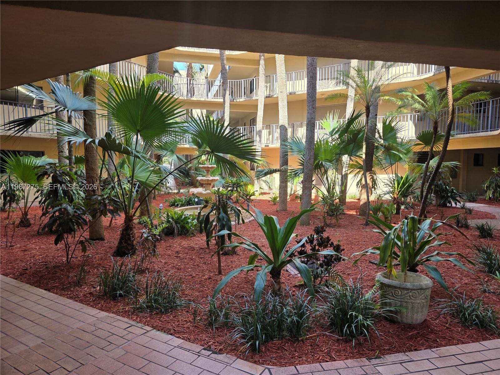 An open-air courtyard features a central fountain, palm trees, and red mulch landscaping — 8615 NW 8th St # 319, Miami FL 33126, MIAMI, FL
