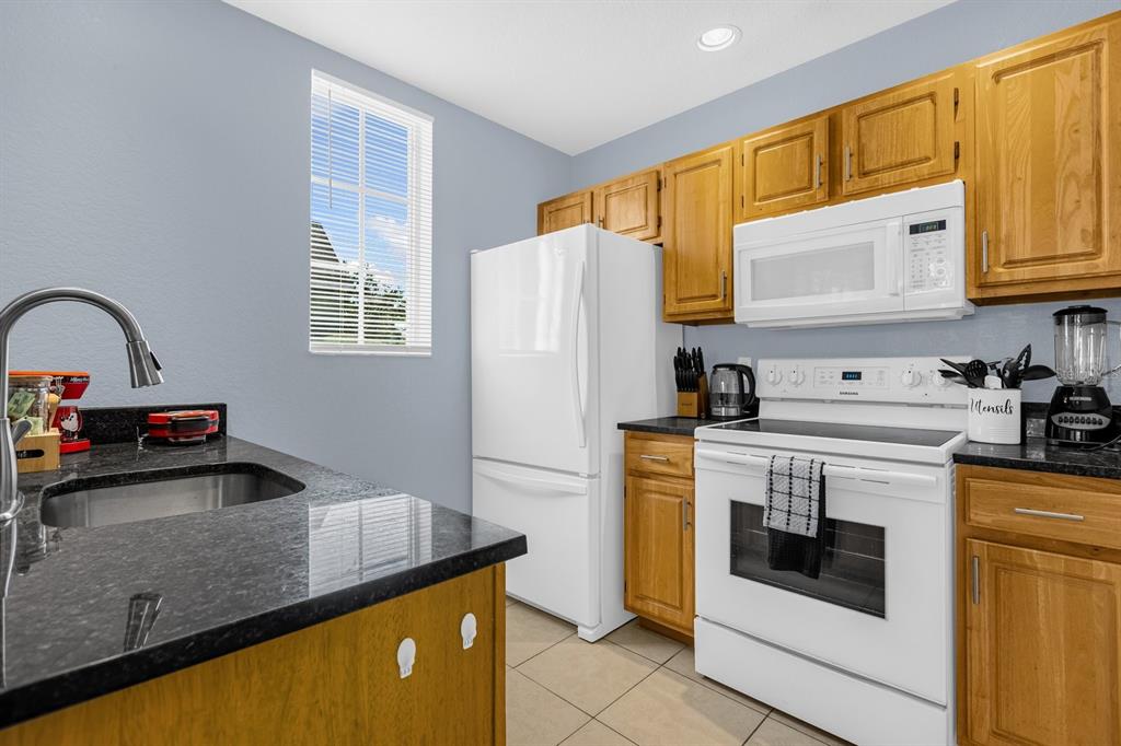 A kitchen features light wood cabinets, dark granite countertops, and white appliances against blue walls — 4013 VENETIAN BAY DRIVE UNIT 107, KISSIMMEE, FL