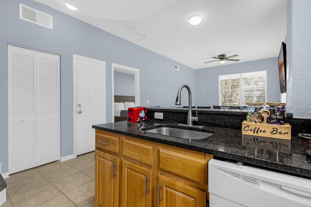 A kitchen island with a sink and dark countertops sits before a light blue room — 4013 VENETIAN BAY DRIVE UNIT 107, KISSIMMEE, FL