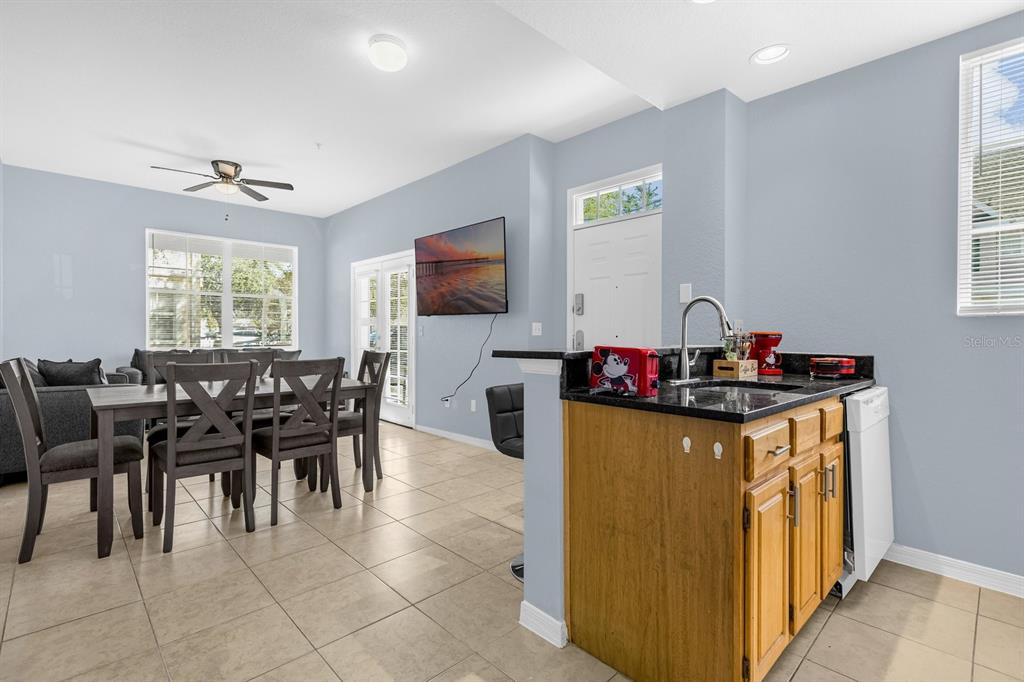A kitchen with wood cabinets and a granite countertop overlooks a dining area and living room — 4013 VENETIAN BAY DRIVE UNIT 107, KISSIMMEE, FL
