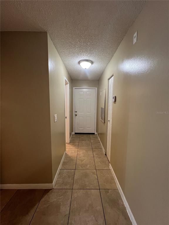 A hallway with beige walls, tile flooring, a ceiling light, and a white entry door — 709 SECRET HARBOR LN UNIT 207, LAKE MARY, FL