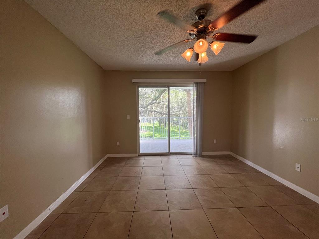 An empty room features beige walls, tiled floors, a ceiling fan, and sliding glass doors — 709 SECRET HARBOR LN UNIT 207, LAKE MARY, FL