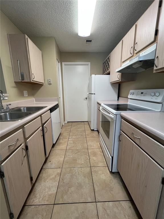 A galley kitchen features light wood cabinets, beige countertops, tile flooring, and white appliances — 709 SECRET HARBOR LN UNIT 207, LAKE MARY, FL