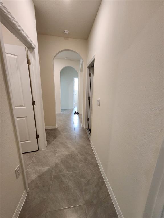 A hallway with light-colored walls, tiled floors, and arched transitions leads to another room — 6930 AUDOBON OSPREY COVE, HARMONY, FL