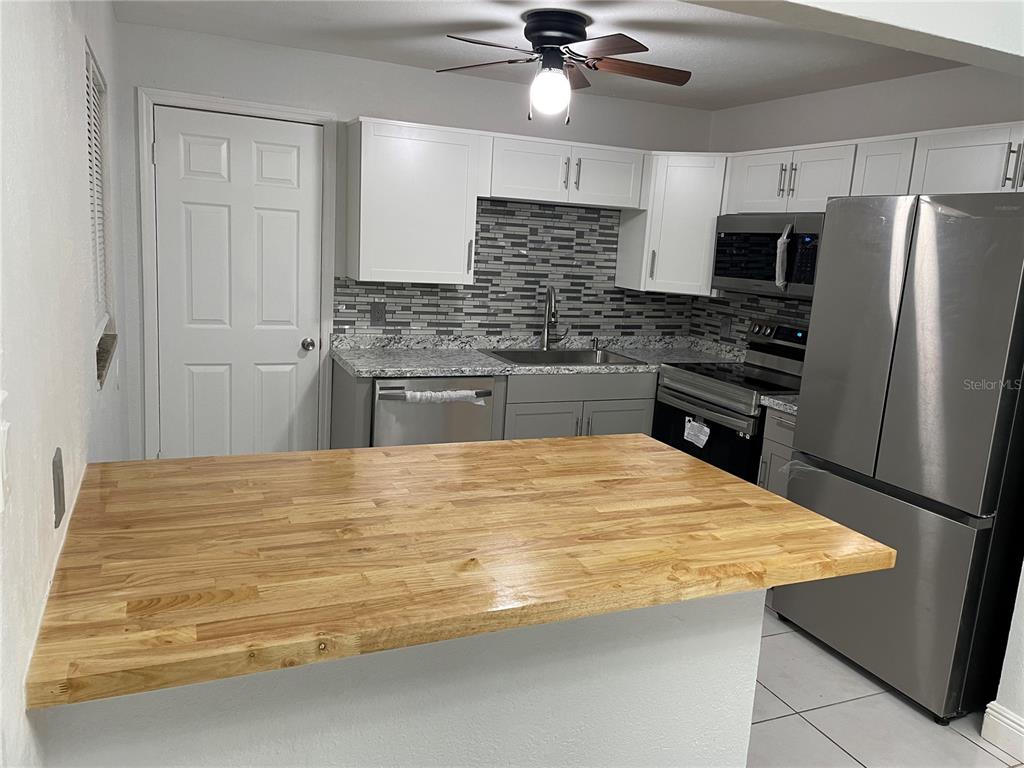 A kitchen features white cabinets, stainless steel appliances, a tiled backsplash, and a wood countertop — 44 S EDGEMON AVENUE, WINTER SPRINGS, FL