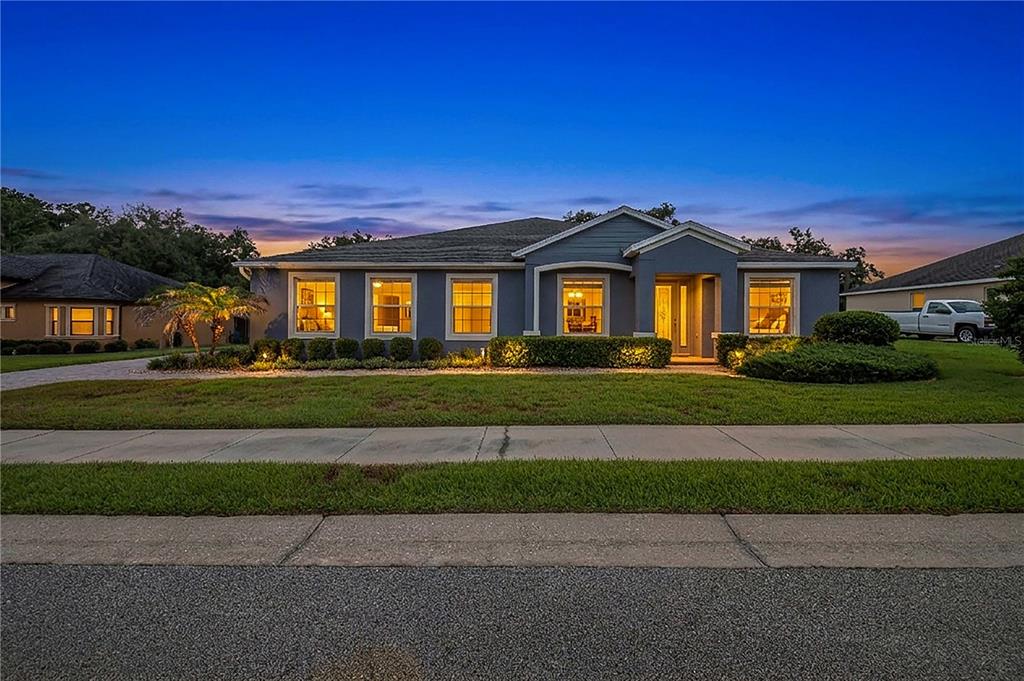 A single-story gray house with a front porch and illuminated windows at dusk — 1020 LENA RUN COURT, WINTER HAVEN, FL