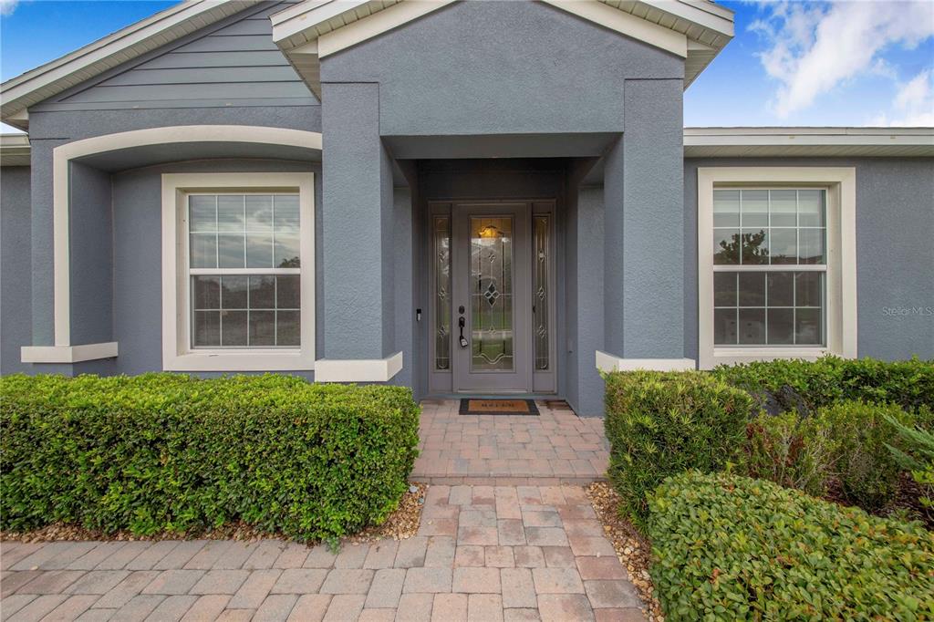 The front entrance of a gray house features a paved walkway and manicured green hedges — 1020 LENA RUN COURT, WINTER HAVEN, FL