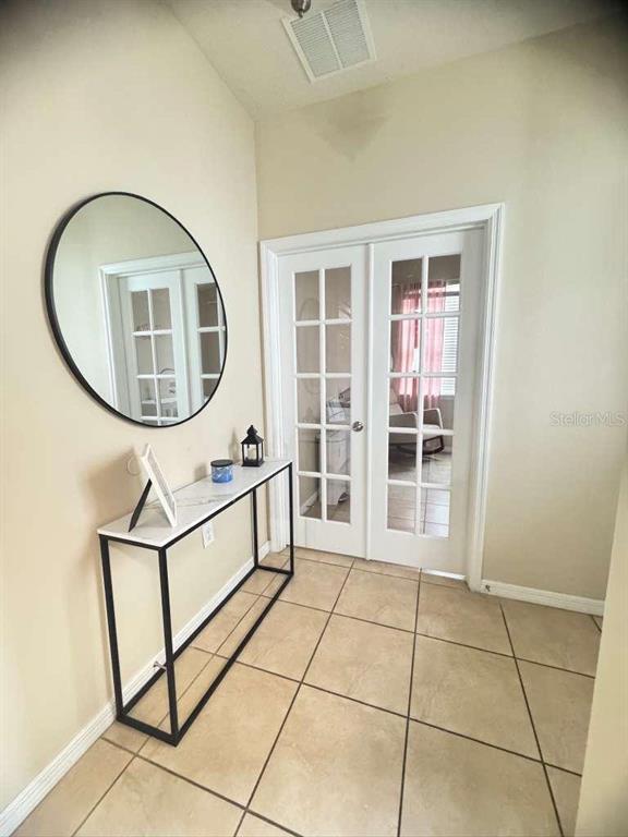 A foyer features a round mirror, a console table, and white French doors on tiled flooring — 2515 NOUVEAU WAY, KISSIMMEE, FL